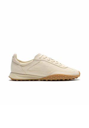 Zapatilla beige de corte bajo con cordones y suela marrón claro texturizada, mostrada de perfil sobre fondo blanco.