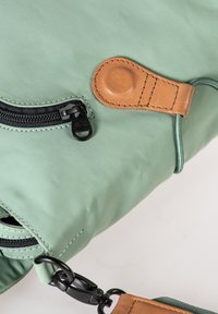 Grüne Stofftasche mit schwarzem Reißverschluss, Lederakzenten und metallischemverschluss. Glatte Textur, kantiges Design und kontrastierende Nähte.