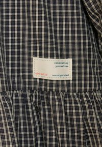 Kockás anyag gyűrt varrással és varrt, téglalap alakú címkével, amelyen az "ünnepelve önmagatokat odd molly uncorporated" felirat szerepel