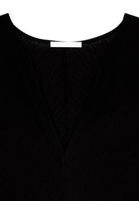 Nærbillede af sort tekstureret stof med en dyb V-udskæring og et hvidt mærke syet på bagkraven.