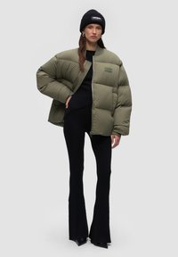 Puffer jacket in olive green, quilted design, zip closure, ribbed knit inner layer, paired with black flared pants and a black beanie.