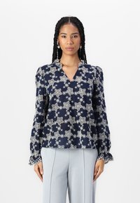 Blusa blu navy con intricati ricami floreali bianchi, caratterizzata da scollatura a V, colletto con volant e maniche lunghe con polsini scallop.