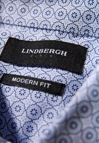 Colletto di camicia con motivo blu con etichette "LINDBERGH BLACK" e "MODERN FIT", disegni floreali e tessuto liscio e strutturato.