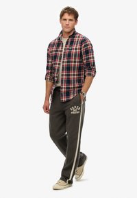 Geruite shirt in rood, marineblauw en wit; lichtgrijze t-shirt eronder; grijze sweatpants met witte zijstrepen en logo; beige sneakers.