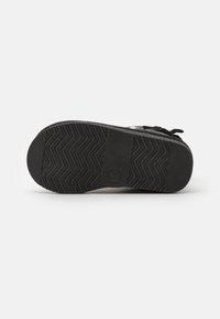 Suela de zapato de goma negra con un patrón de tracción en zigzag y un detalle de marca circular. Superficie texturizada con bordes reforzados para mayor durabilidad.