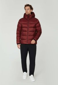 Mørkerød pufferjakke med hætte, med lynlås og sidelommer, parret med sorte bukser og hvide sneakers. Glat tekstur.