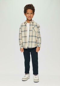 Button-down Flanellhemd in Creme mit blauen und grünen Karos, kombiniert mit navyblauen Hosen und weißen Sneakers mit grauen Akzenten.