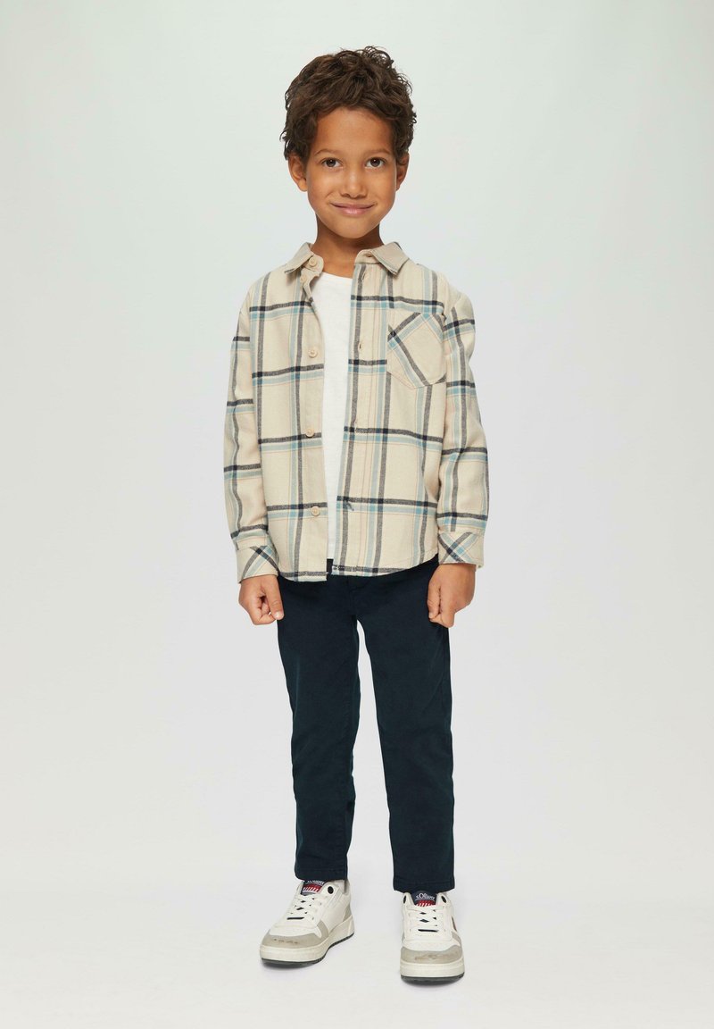 Button-down Flanellhemd in Creme mit blauen und grünen Karos, kombiniert mit navyblauen Hosen und weißen Sneakers mit grauen Akzenten.