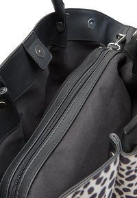 Vista interna di una borsa a fantasia leopardata che mostra una grande pochette nera con zip e chiusure a scatto magnetico.
