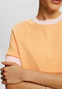 Kortærmet sweater i ferskenfarve med ribbet pink krave og manchetter. Blød tekstur med synlige syninger og afslappet pasform.
