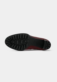 Scarpa in suede rossa con suola in gomma nera testurizzata, caratterizzata da profonde scanalature per garantire aderenza, punta arrotondata e hardware minimale.