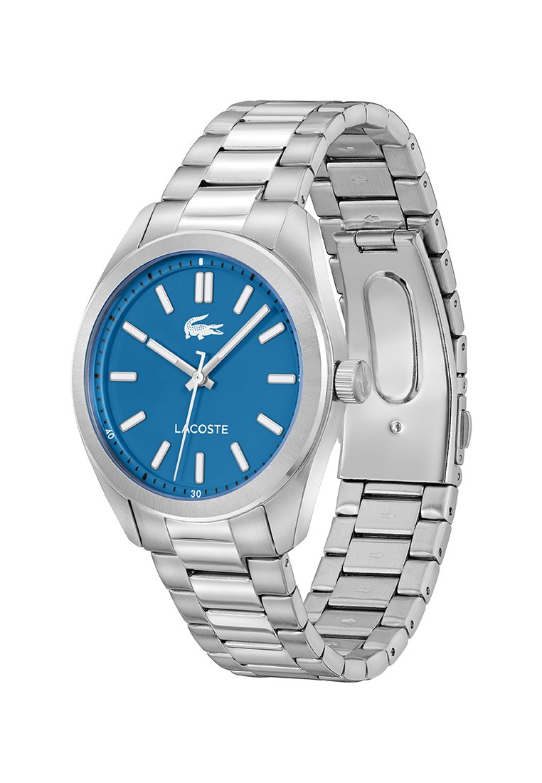 Reloj de pulsera de metal plateado con esfera azul, marcadores de hora plateados, tres manecillas, logo de Lacoste y pulsera de metal entrelazada abierto.
