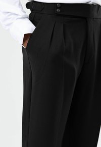 Pantalon noir plissé avec un tissage texturé, doté d'une taille haute et de deux boutons. Le design met en valeur des lignes nettes et une coupe structurée.