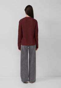 Suéter de punto burdeos con un acabado texturizado, mangas largas y cuello redondo, combinado con jeans de pierna ancha grises y calzado beige.