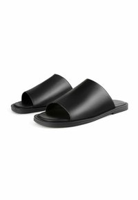 Schwarze offene Sandalen mit glattem Lederobermaterial, flacher Sohle und minimalistischem Design. Die Sandalen verfügen über ein breites Band über dem Fuß für einen sicheren Sitz.