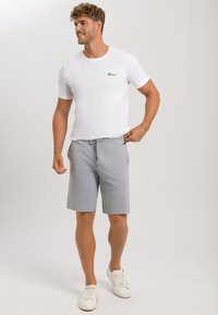 Vit t-shirt med rund hals och en liten svart logotyp, tillsammans med grå shorts med dragsko. Lätt material, avslappnad passform och vita sneakers.