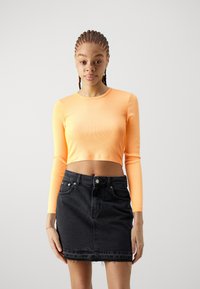 Pikend varrukatega oranž ribikangasest crop-top, mis on kombineeritud kõrge talje ja ees taskutega musta denim-seelikuga, millel on frayed ääred.
