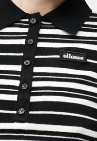 Πουκάμισο πόλο με μαύρες και λευκές ρίγες, με μαύρο γιακά και πέντε κουμπιά, που φέρει μαύρο ορθογώνιο λογότυπο "ellesse" στο στήθος.