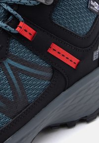 Αδιάβροχο παπούτσι πεζοπορίας σε μπλε και μαύρο με κόκκινες θηλιές για δεσίματα, αναπνεύσιμο δίχτυ και υφή γκρι σόλας.