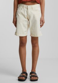 Shorts en denim couleur crème avec des ourlets roulés, un design à cinq poches et une taille standard. Assortis à des sandales plates noires.
