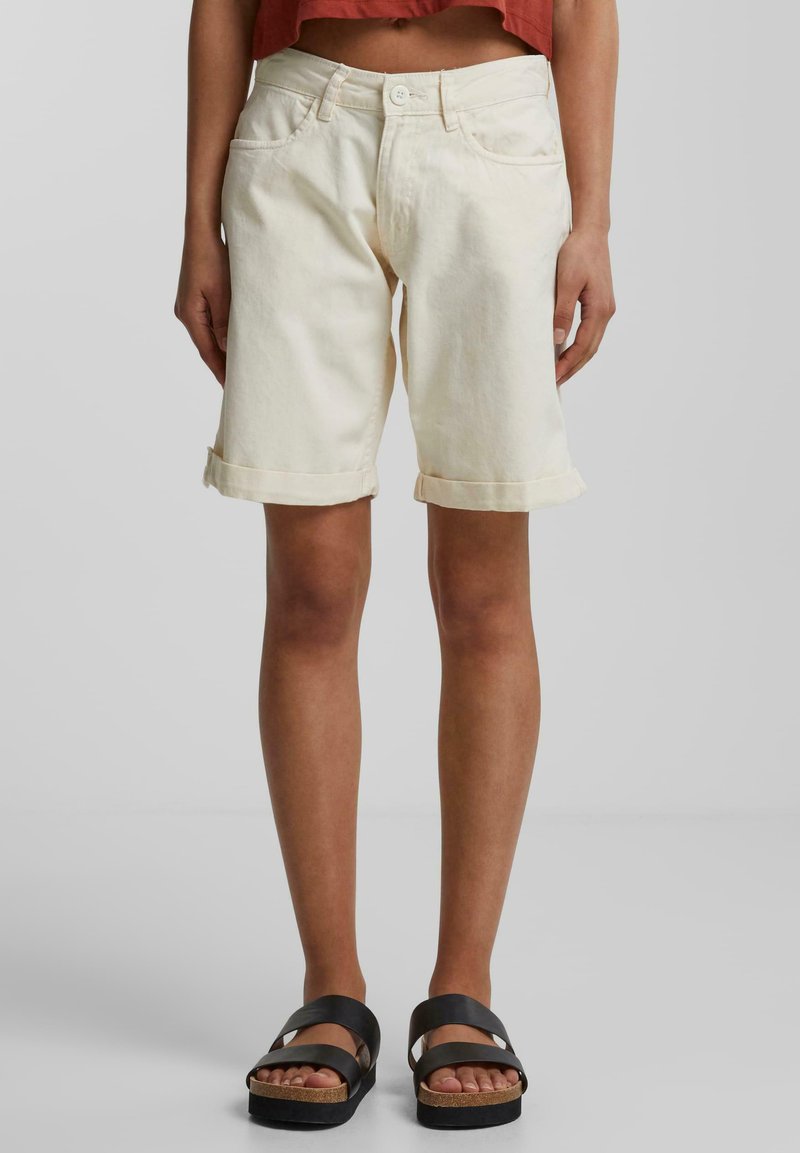 Shorts en denim couleur crème avec des ourlets roulés, un design à cinq poches et une taille standard. Assortis à des sandales plates noires.