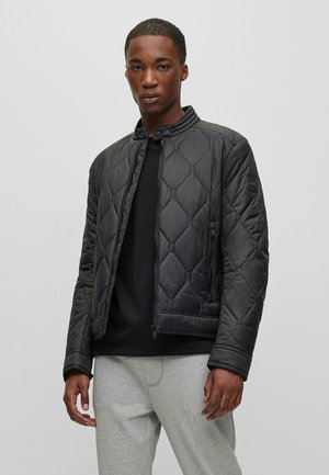 Black quilted jacket with a standing collar, zip closure, and side pockets. Features a textured surface and minimalistic design.