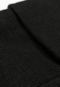Tessuto nero lavorato a maglia con una superficie testurizzata, caratterizzato da sezioni sovrapposte che creano un aspetto a strati. Materiale liscio e flessibile.