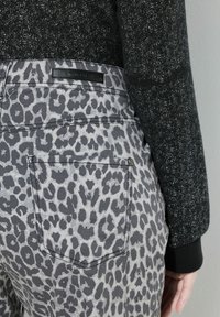 Jeans con stampa leopardata grigia con taschino posteriore, abbinati a un maglione nero testurizzato con scollo rotondo e polsini a costine.