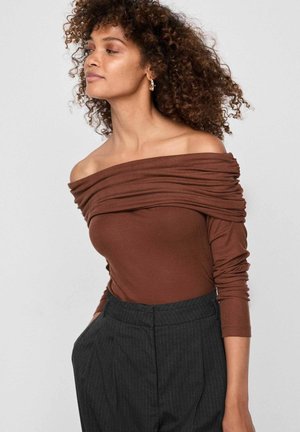 Brun ribbad off-shoulder topp med draperingsdetalj och långa ärmar, tillsammans med mörka randiga högmidjade byxor.