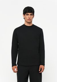 Svart langermet T-skjorte laget av myk kvalitet, med rund hals og vanlig passform. Minimalistisk design uten synlige mønstre eller detaljer.
