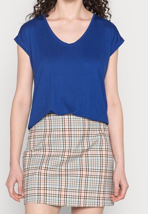 Vrouw draagt een blauwe V-hals top met korte mouwen en een pastel geruite high-waisted minirok.