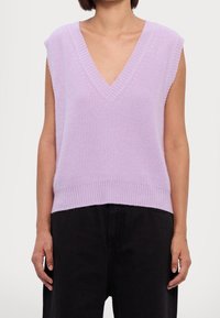 Top smanicato lilla in maglia con scollo a V profondo, trama a coste e vita aderente, abbinato a pantaloni neri a gamba larga.