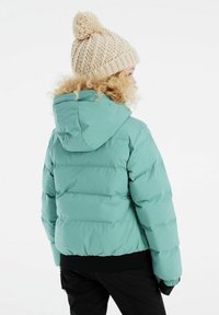 Pufferjacke in hellem Petrol mit Kapuze, ausgestattet mit horizontalen gesteppten Abschnitten und einem schwarzen gerippten Saum. Strickmütze in Creme mit einem Pompon oben.