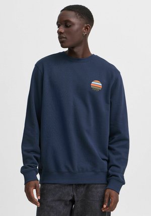 Marinblå sweatshirt med ribbad crewhals, med ett cirkulärt grafiskt mönster i orange och vitt. Tillverkad av texturerat tyg.