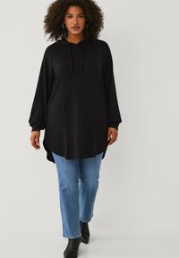 Sort hættetrøje med lange raglanærmer, frontlomme og sideslids. Blandet med lyseblå jeans og sorte ankelstøvler.