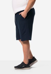Pantaloni corti blu navy con elastico in vita e cordoncino, dotati di tasche laterali. Indossati con scarpe da ginnastica nere e una maglietta bianca.