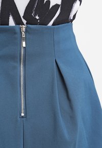 Gonna blu in poliestere con chiusura frontale a zip e dettagli plissettati, dalla texture liscia e design aderente.