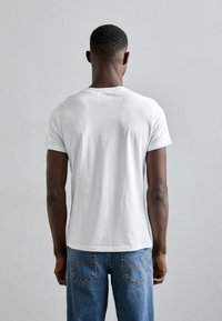 Λευκό βαμβακερό t-shirt με κοντά μανίκια, στρογγυλό λαιμό και χαλαρή εφαρμογή, συνδυασμένο με μπλε τζιν παντελόνι που διαθέτει πίσω τσέπες με διακοσμητική ραφή.