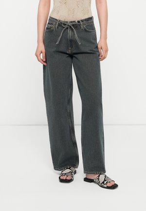 Løse, høyt liv grå denimjeans med snor i livet, frontlommer og kontrastsøm. Kombinert med svart-hvite mønstrede sandaler.