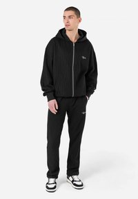 Black corduroy zip-up hoodie with a drawstring hood and front pockets, paired with matching pants. Features logo embroidery on both.
