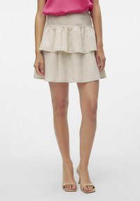 Gonna beige a balze con vita arricciata, realizzata in un tessuto leggero e testurizzato, con un design svasato, abbinata a tacchi aperti neutri.