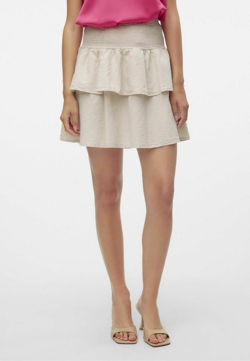 Gonna beige a balze con vita arricciata, realizzata in un tessuto leggero e testurizzato, con un design svasato, abbinata a tacchi aperti neutri.