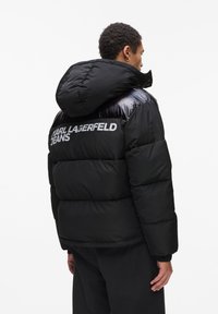 Zwarte pufferjack met een glanzende afwerking en een oversized capuchon. Bevat het logo "KARL LAGERFELD JEANS" op de achterkant. Dikke, gestikte ontwerp.