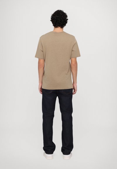 T-shirt en coton beige à manches courtes et col rond, associé à un jean en denim bleu foncé et des baskets blanches. Détails visibles au dos.