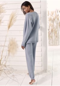 Hellgraues Loungewear-Set bestehend aus einem lässig geschnittenen Pullover und schmal zulaufenden Hosen. Weicher Stoff mit gerippten Bündchen und Logodetail an den Hosen.