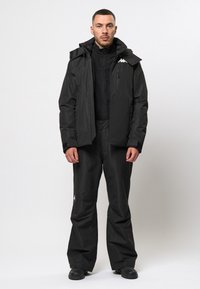 Zwarte buitenkledingset bestaande uit een jas en broek, gemaakt van een mat materiaal, met een ritssluiting aan de voorkant, capuchon en een logo-accent op de borst.