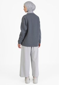 Sudadera gris de gran tamaño con mangas largas, acompañada de pantalones anchos de color gris claro y zapatillas blancas con detalles en rosa.