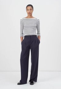 Gestreiftes langärmliges Oberteil mit einem Bootsausschnitt in Weiß und Marineblau, kombiniert mit hoch taillierten, weiten Marineblau-Hosen. Schwarze Schuhe runden den Look ab.