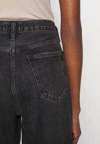 Mustat denim-farkut, joissa on korkea vyötärö, näkyvät saumat ja takatasku, matta pinta ja suora lahje.