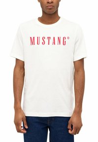 White short-sleeve t-shirt with red "MUSTANG" logo on the chest, made from cotton, featuring a crew neck and a relaxed fit.